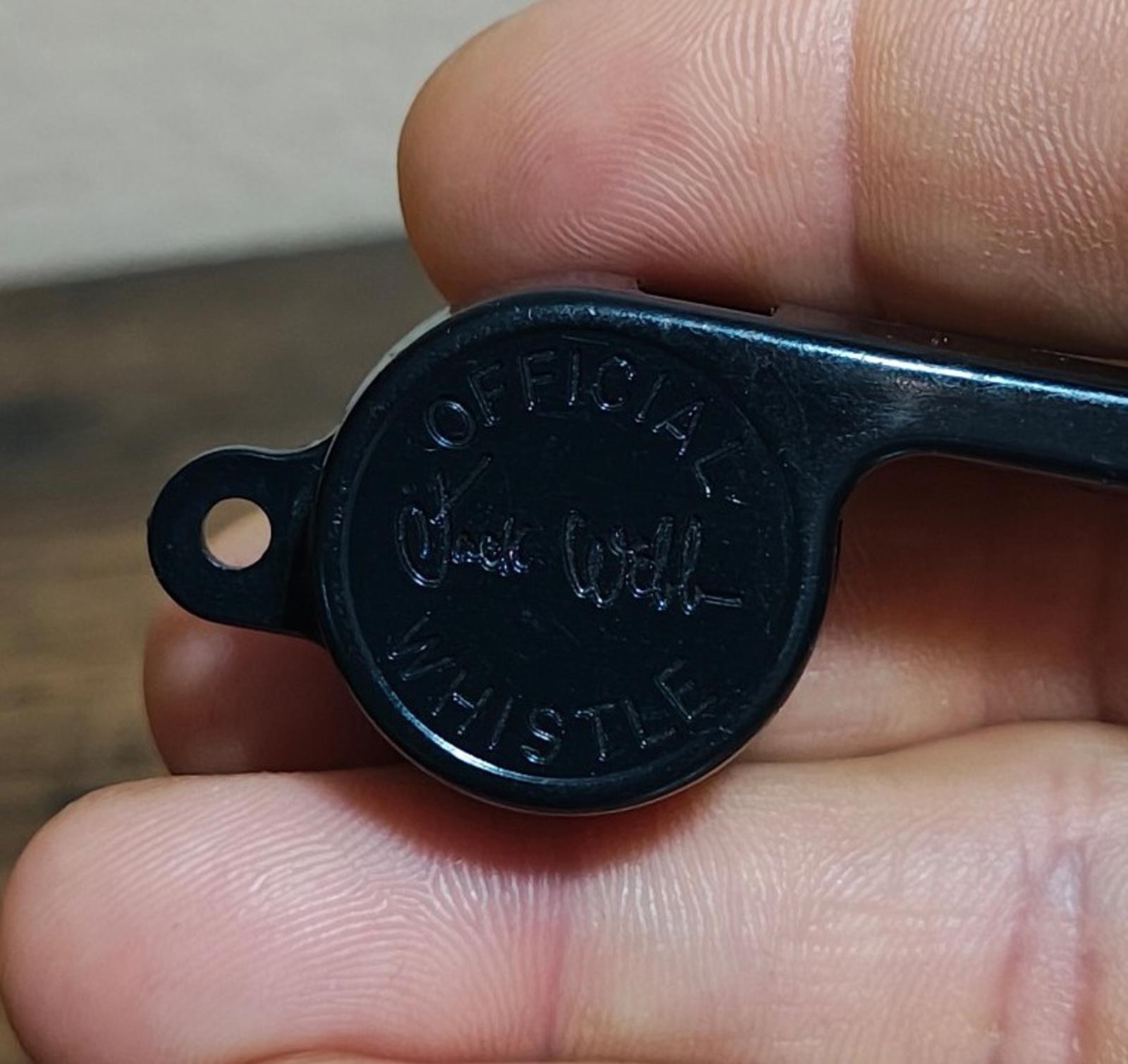 Black whistle end with engraved lettering, close-up held by fingers.