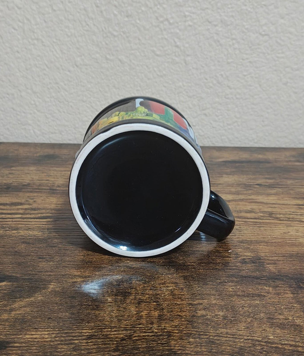 Black ceramic mug with colorful rim accents, open top facing up on tabletop