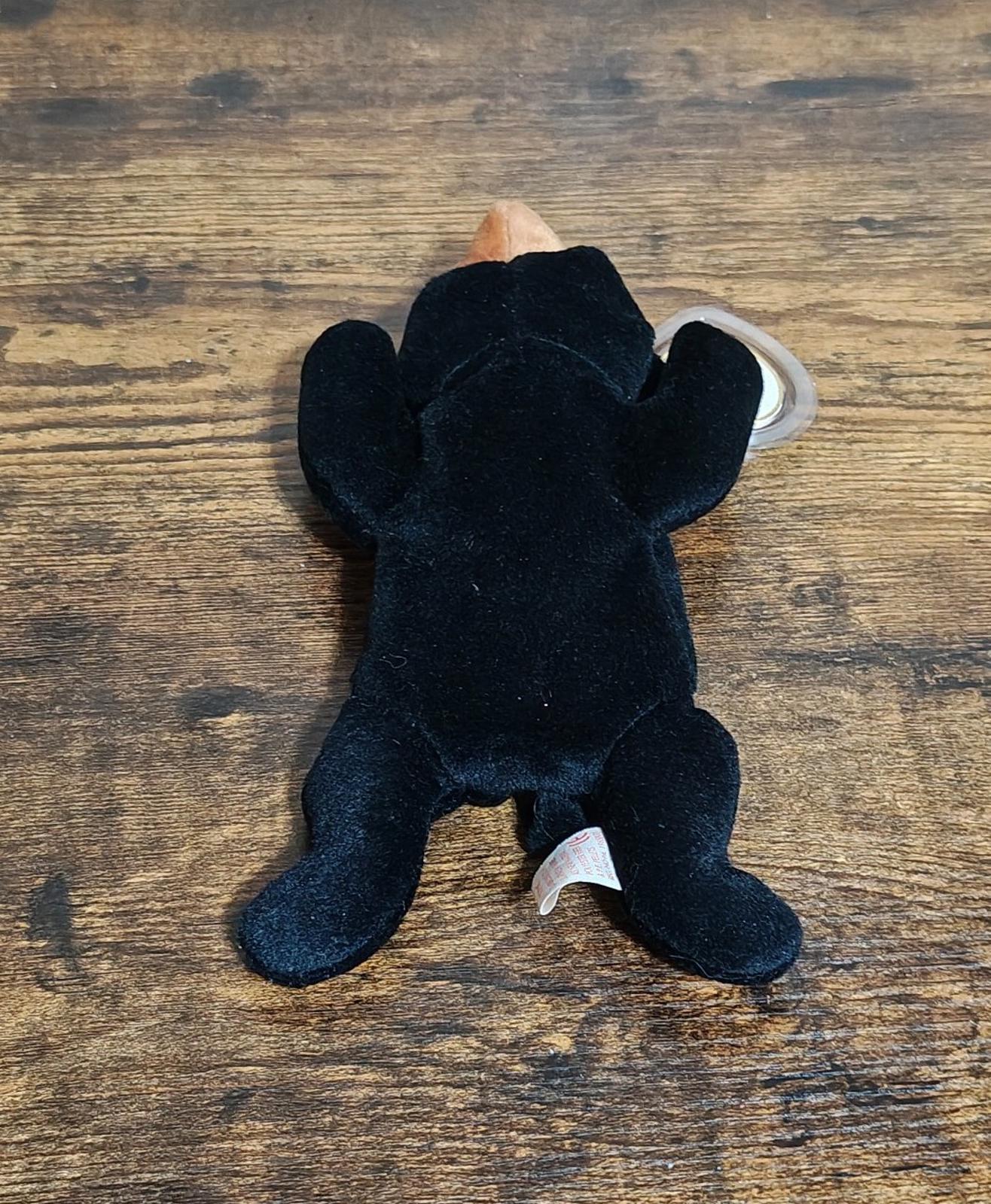 Black plush bear beanbag upright with tan top head and attached white fabric tags