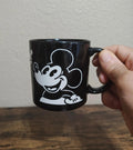Black mug with white Mickey Mouse face graphic and side handle