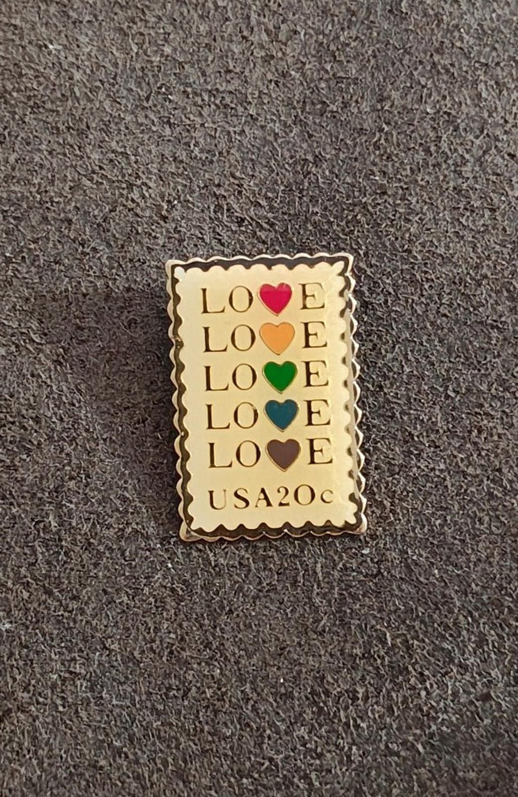 Rectangular gold-tone enamel pin showing repeated “LOVE” text with red, orange, green hearts.