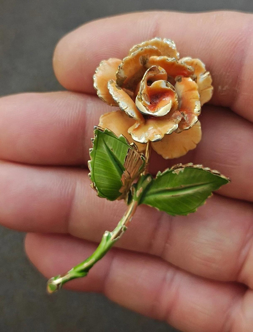 Gold-tone enamel rose and leaf pin, orange petals and green leaves, close-up in hand