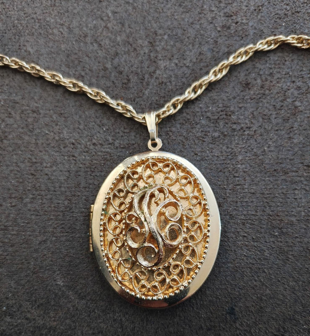 Gold-tone oval locket necklace close-up of ornate filigree front with monogram