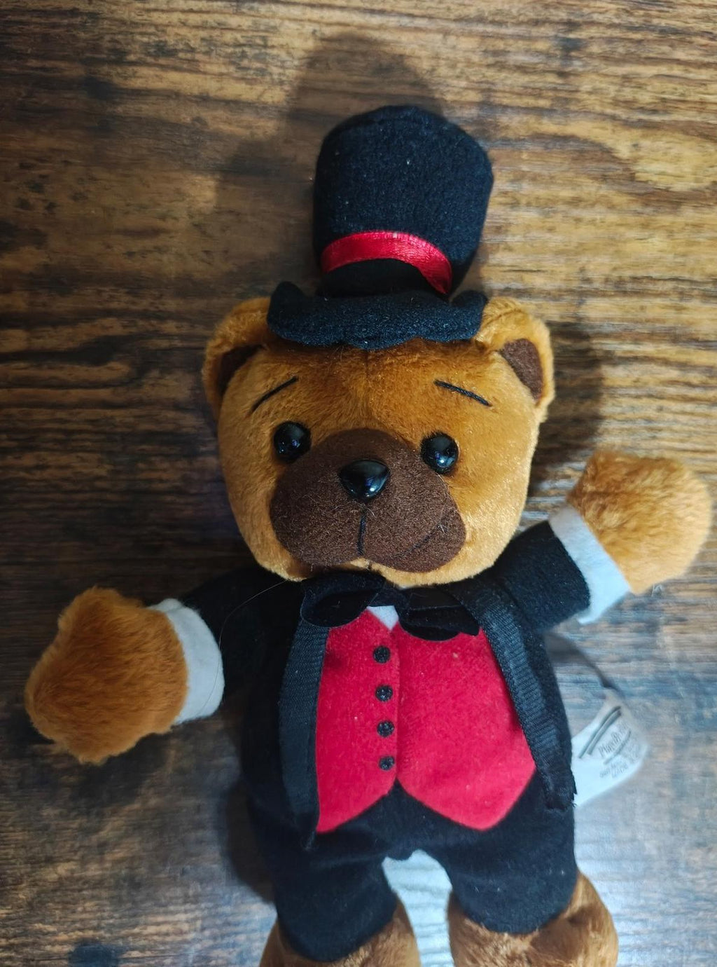 Close-up plush bear face with black top hat, red band, and red vest under tuxedo.