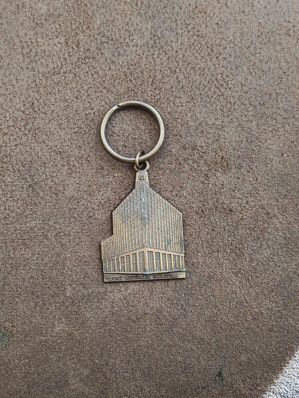 Metal keychain with small building charm and circular ring on concrete background