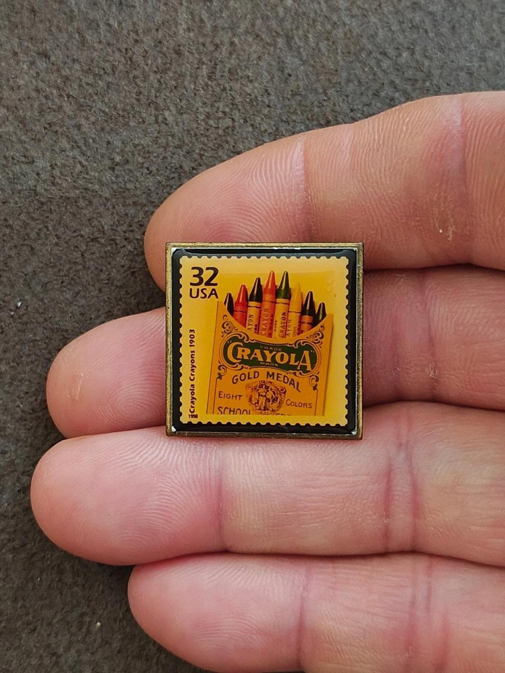 Square gold-tone enamel pin featuring “32 USA” stamp with Crayola Gold Medal crayons