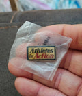 Gold-tone enamel pin reading "Athletes in Action" with red and yellow text, in bag