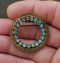 Gold-tone round brooch with blue filigree stones in a wreath frame