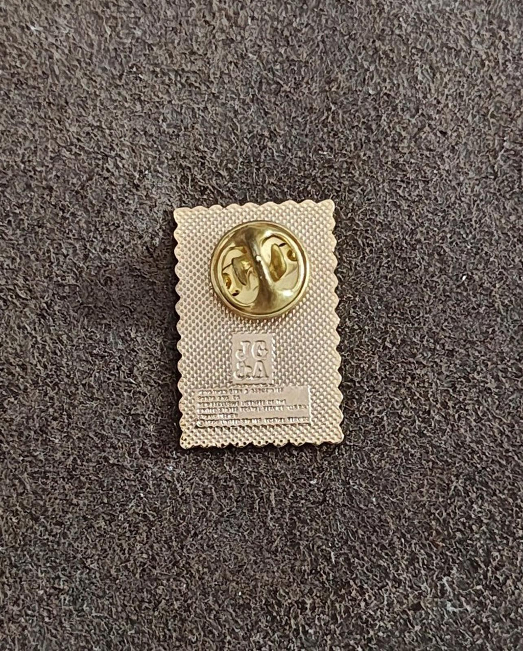 Back of gold-tone enamel pin with circular clasp hardware and stamped markings.
