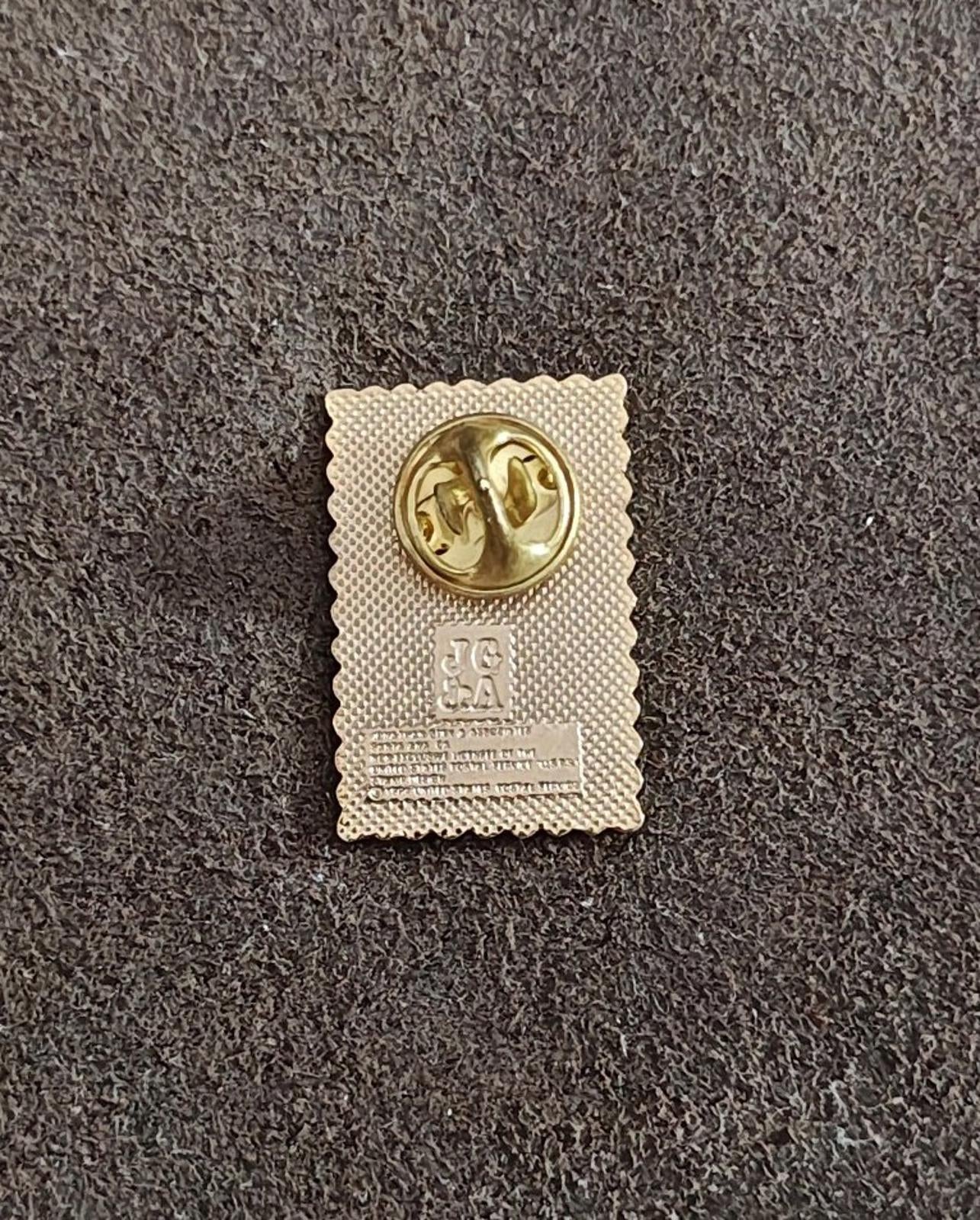 Back of gold-tone enamel pin with circular clasp hardware and stamped markings.