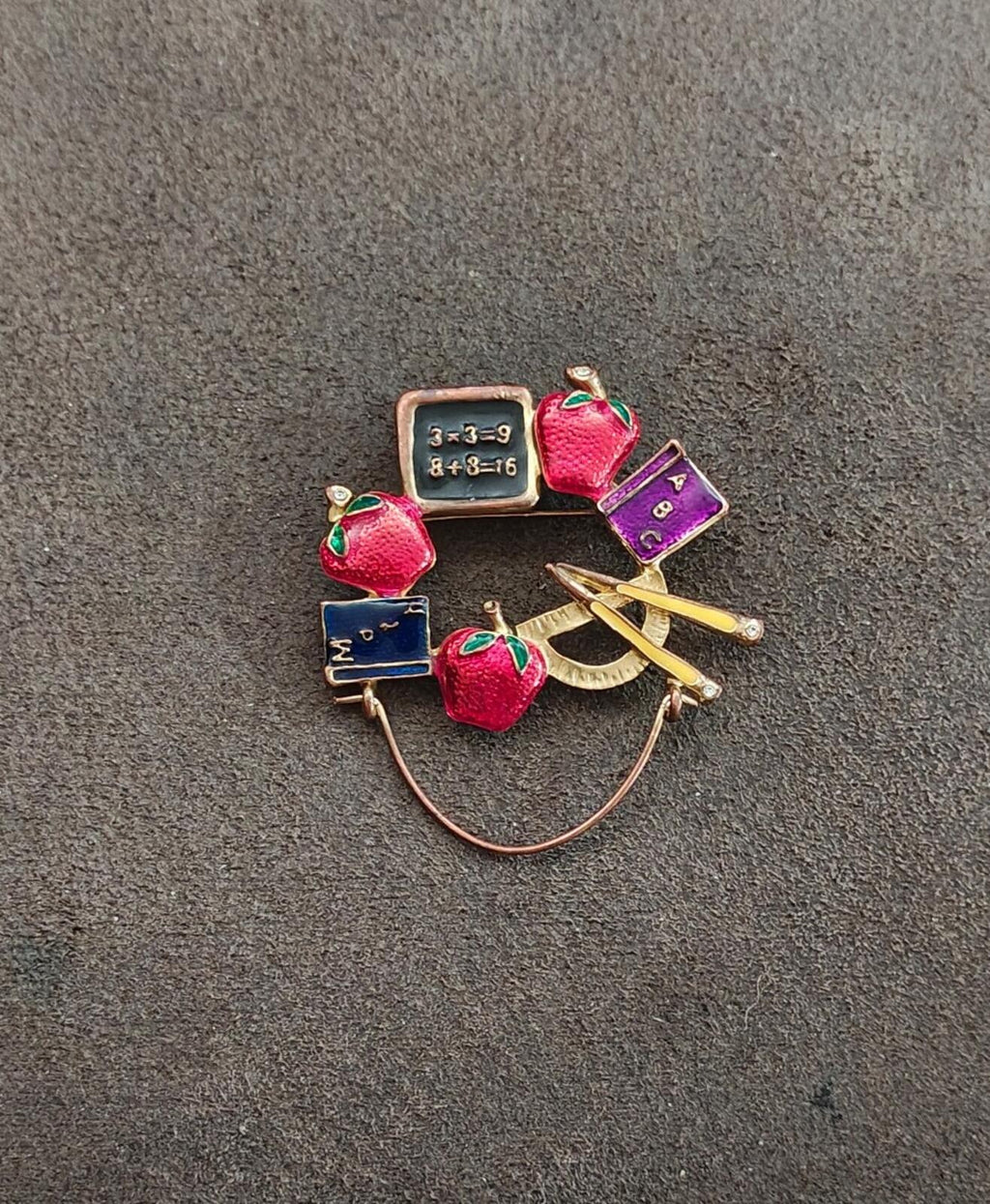 Small school-themed enamel brooch with red apples, books, purple ruler, pencil, and chalkboard.