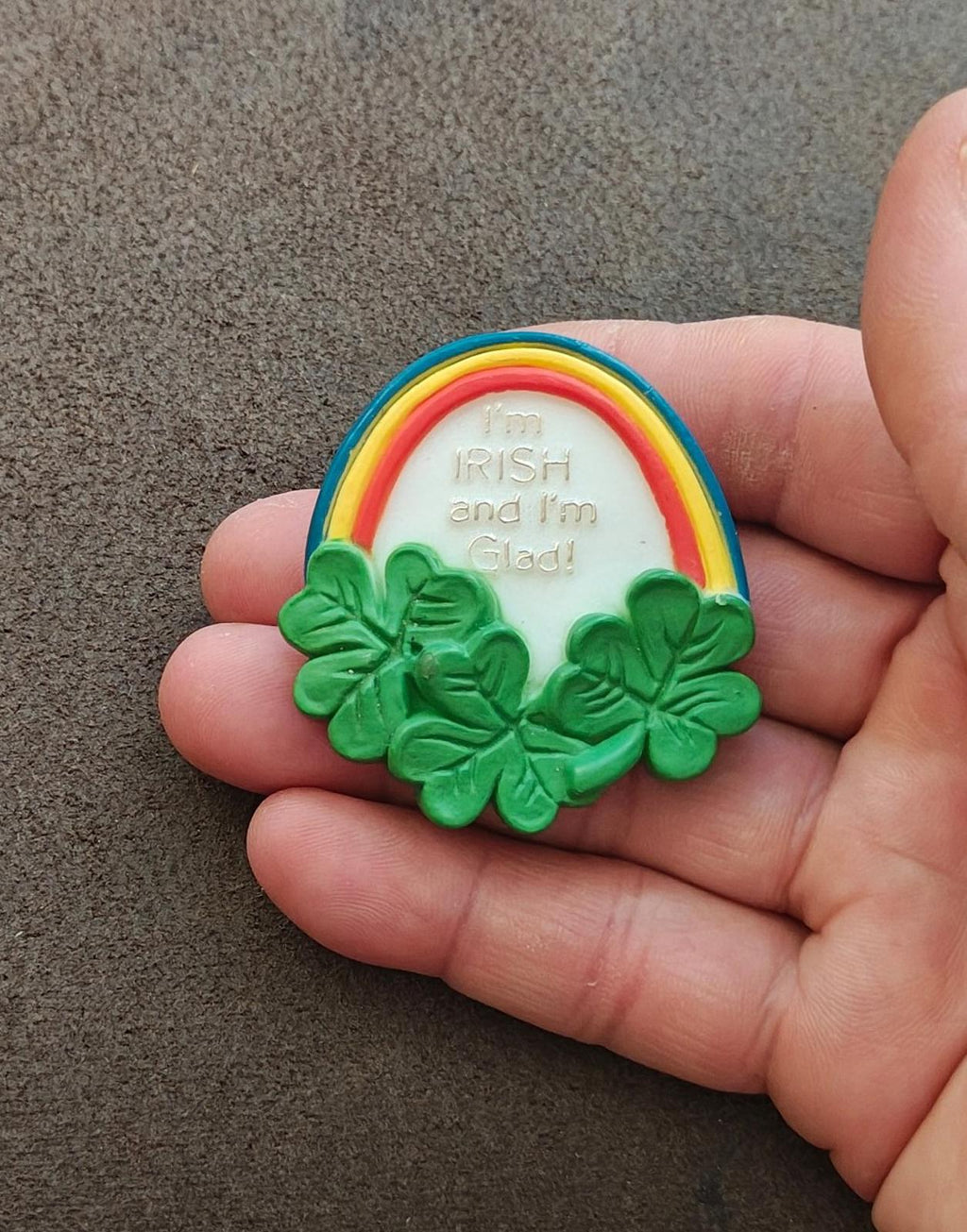 Green rainbow clover brooch pin held in fingers, white center with “I’m Irish and I’m Glad”