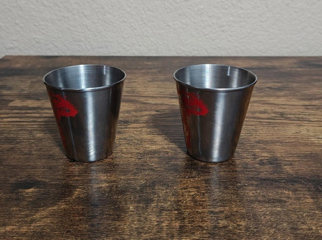 Set of 2 stainless steel shot glasses with minimal red logo markings, front view