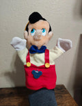 Pinocchio hand puppet with blue eyes, red overall dress, and blue bow tie