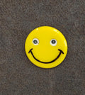Yellow round smiley face pin with glittery eyes and black smile line art