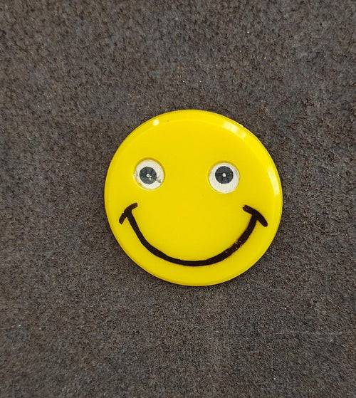 Yellow round smiley face pin with glittery eyes and black smile line art