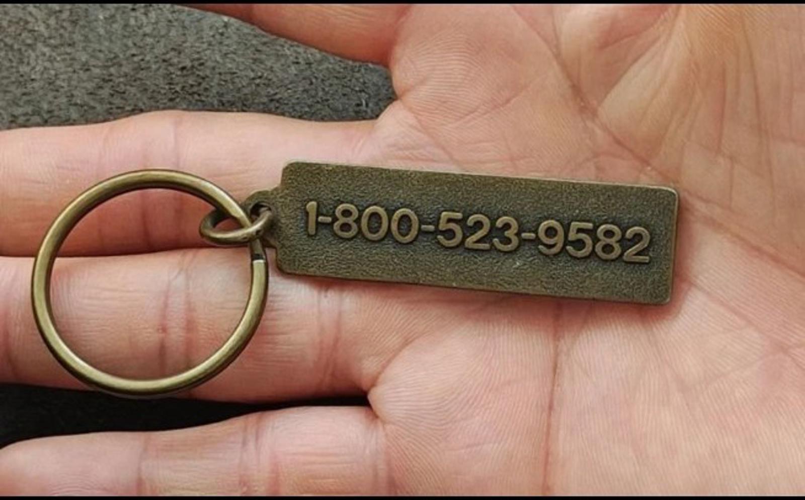 Gold keychain with circular ring and rectangular tag engraved “1-800-523-9582”