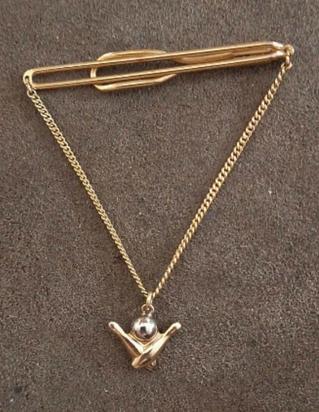 Gold-tone bowling tie bar with chain and pin charm, shown against dark background.