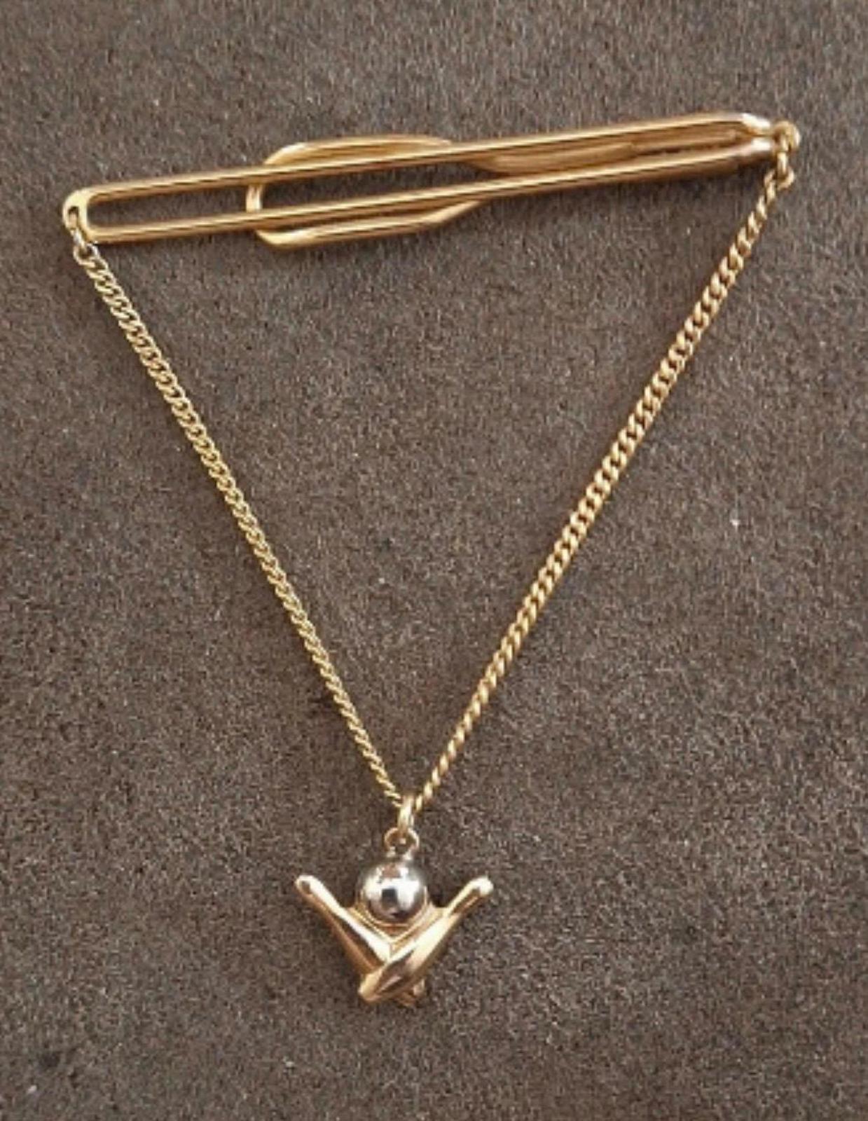 Gold-tone bowling tie bar with chain and pin charm, shown against dark background.