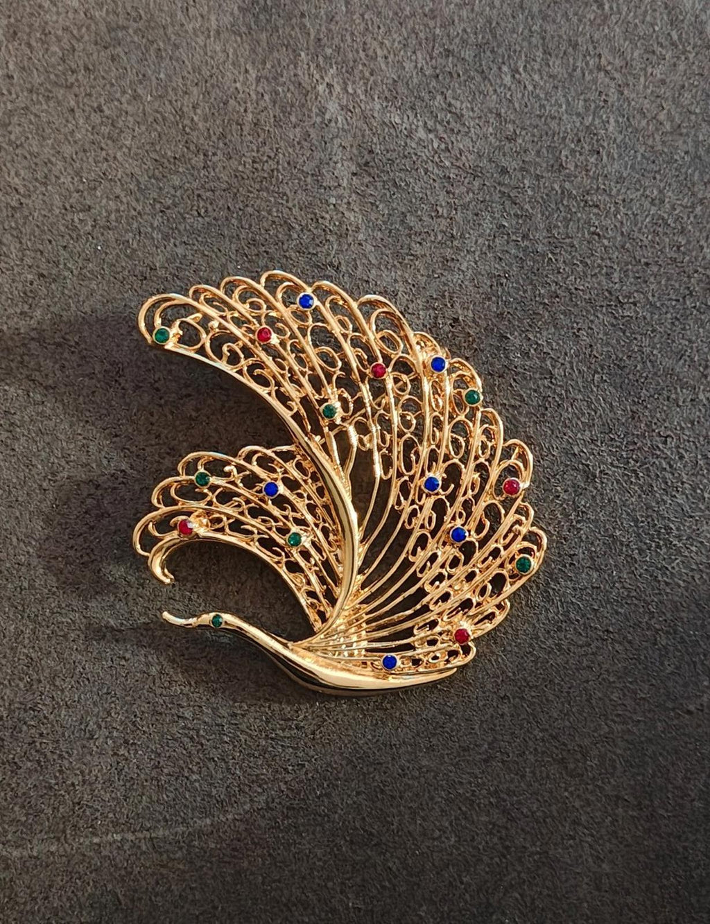 Gold-tone peacock feather brooch pin with multicolor crystals, displayed on dark background.