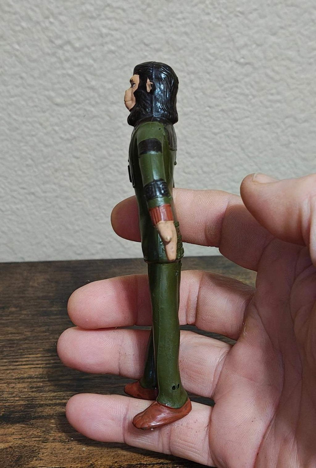Green rubber collectible action figure with black hood, side view showing red wrist bands