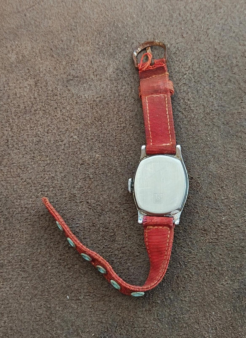 Vintage wristwatch with red strap and metal case, strap tail with eyelets visible.