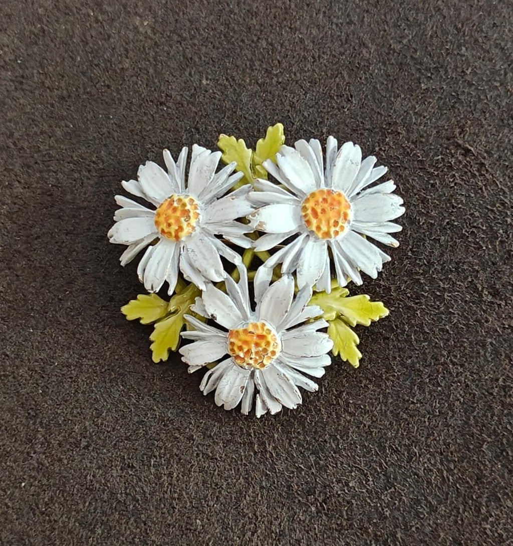 Three-daisy white enamel flower brooch with gold-tone rims and green enamel leaves