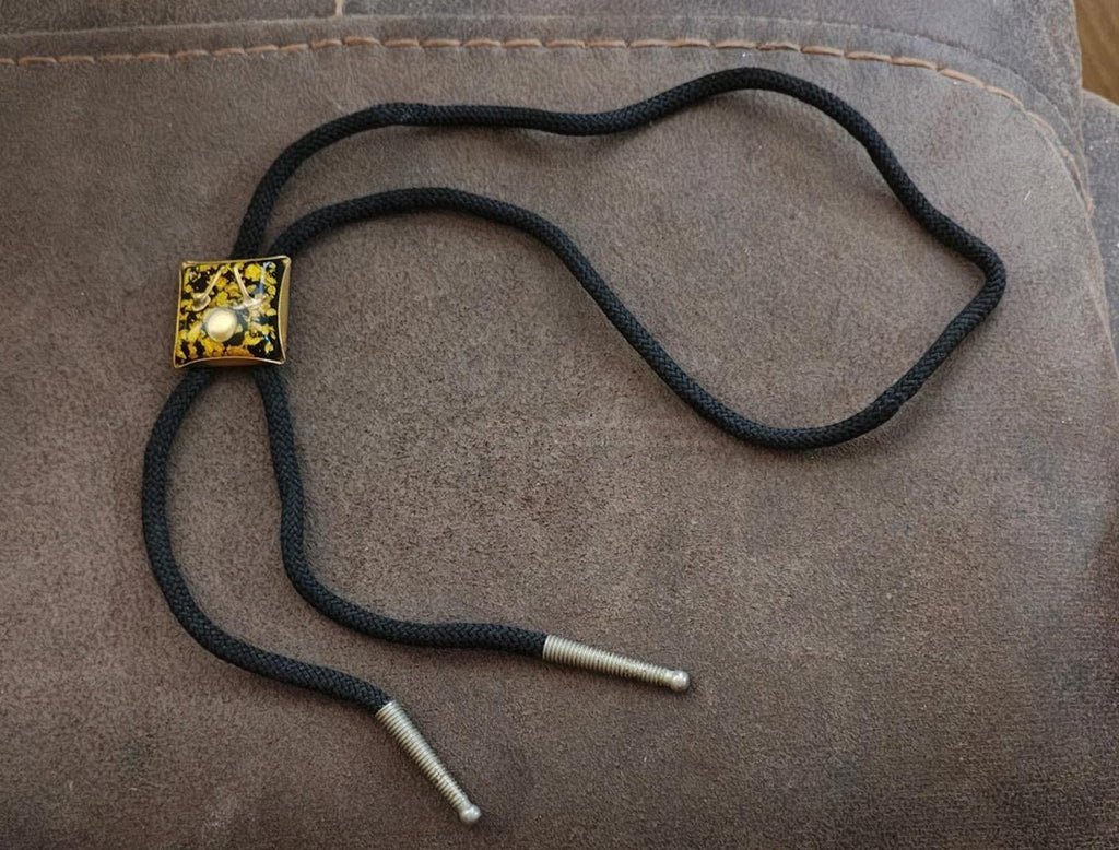 Black braided bolo tie with gold square pendant and two silver-tipped cord ends