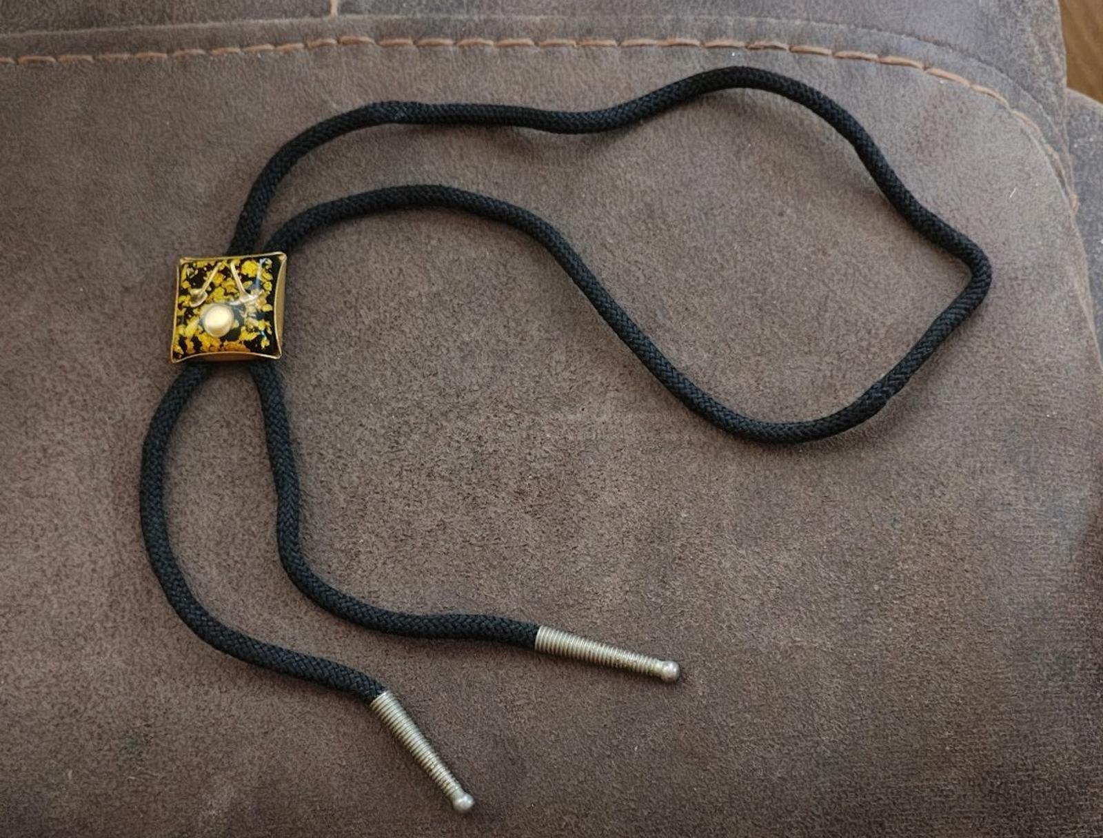 Black braided bolo tie with gold square pendant and two silver-tipped cord ends