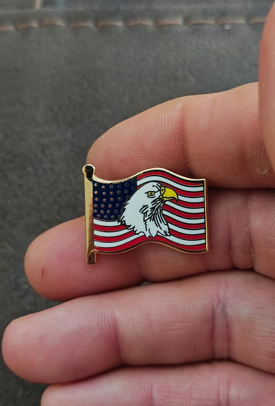 Gold-tone enamel wavy American flag lapel pin with bald eagle, close-up on fingers