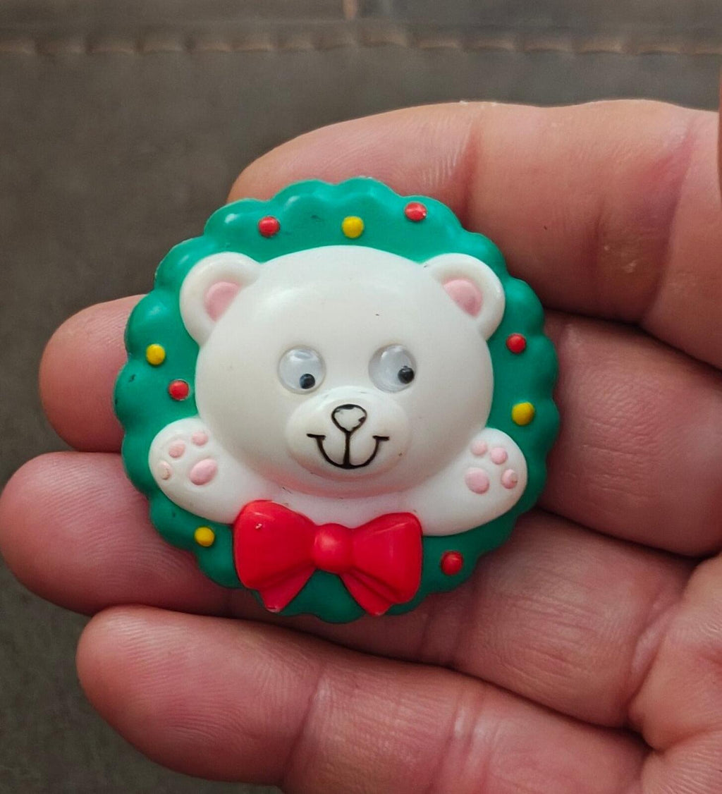 Green bear wreath pin with white bear face, googly eyes, and red bow on hand