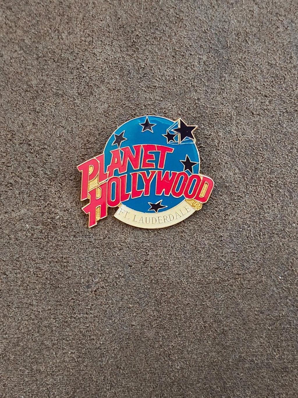 Blue enamel lapel pin with red Planet Hollywood lettering and stars, gold rim.