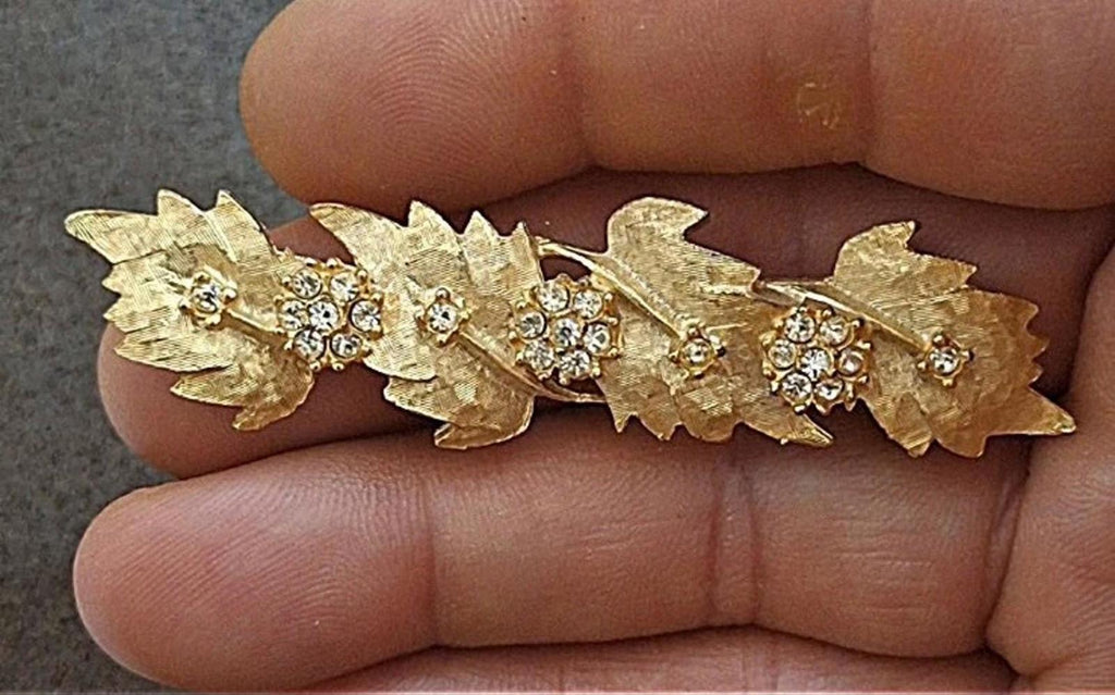 Gold tone leaf rhinestone brooch pin in hand, glittering round crystal centers