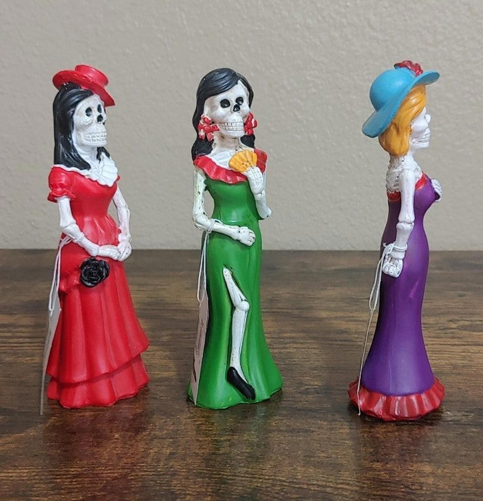 Three Catrina figurines in profile, red, green, and purple dresses