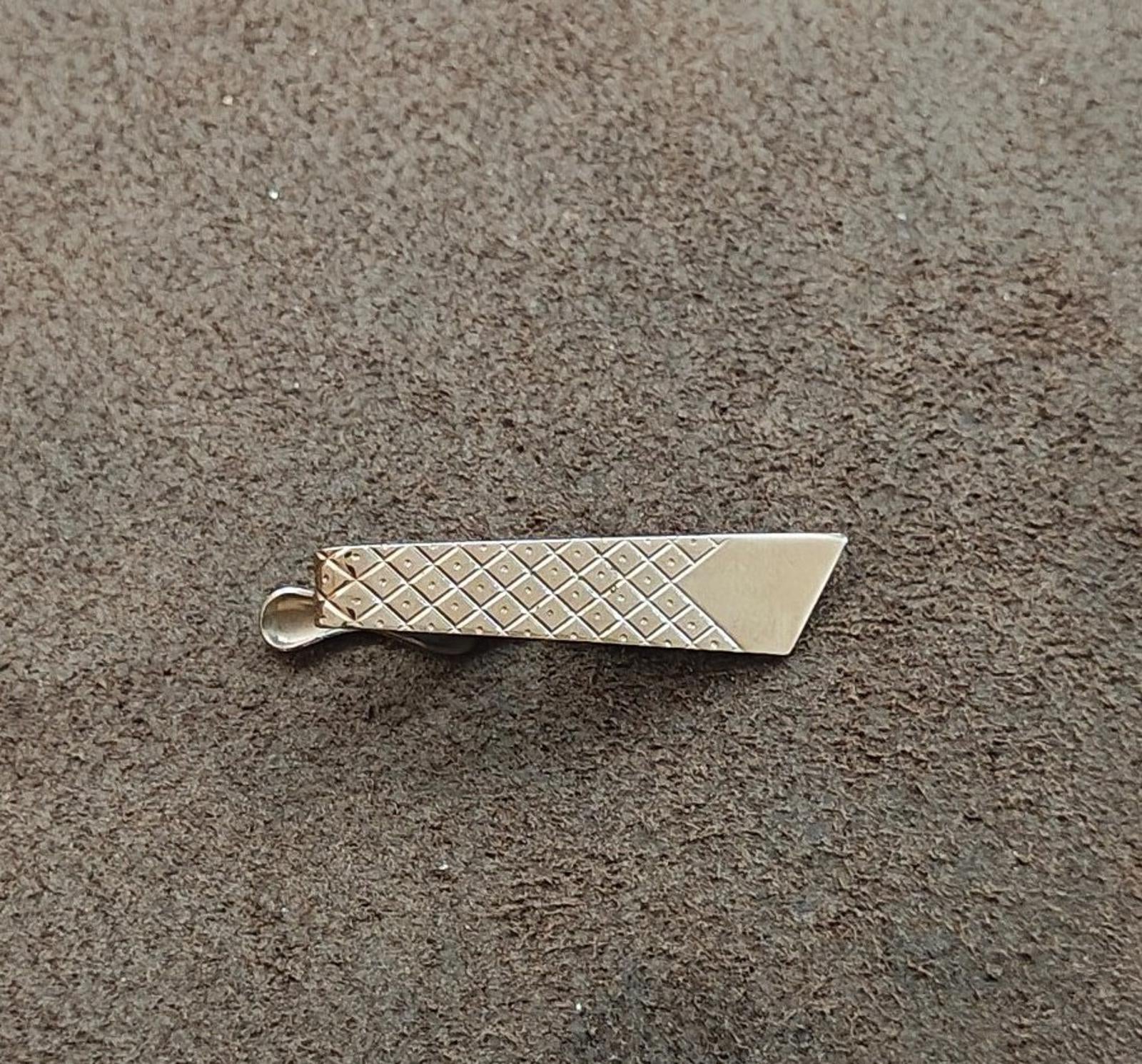 Silver-tone diamond lattice tie bar clip on surface with prong attachment visible