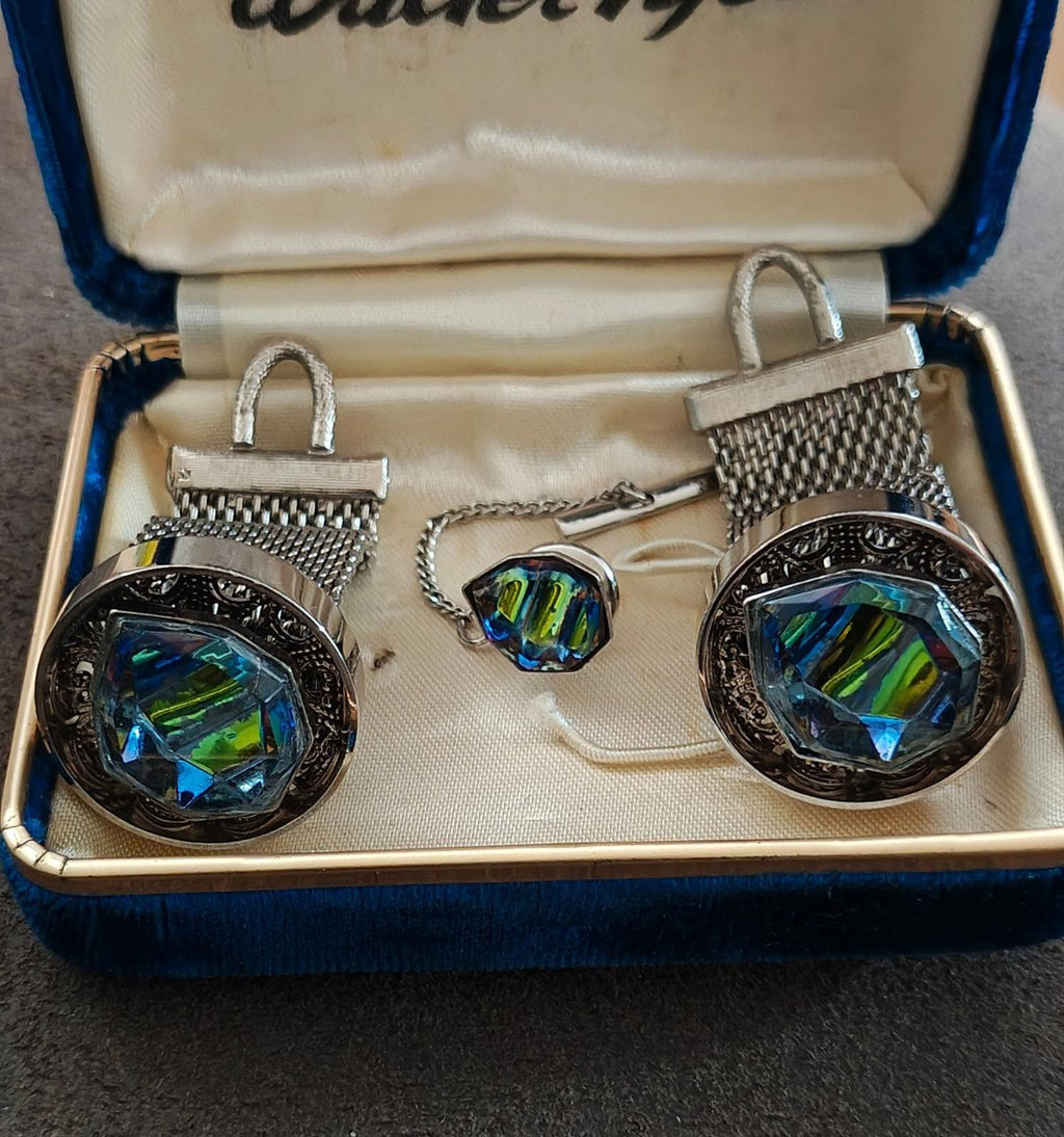 Close-up of iridescent cufflinks and tie tack with silver-toned mesh frames in box