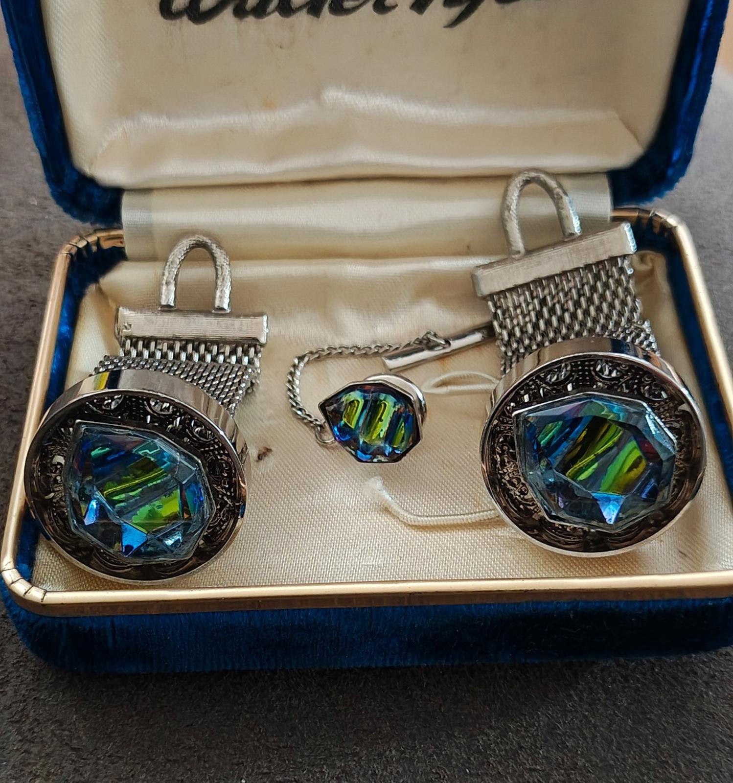 Close-up of iridescent cufflinks and tie tack with silver-toned mesh frames in box