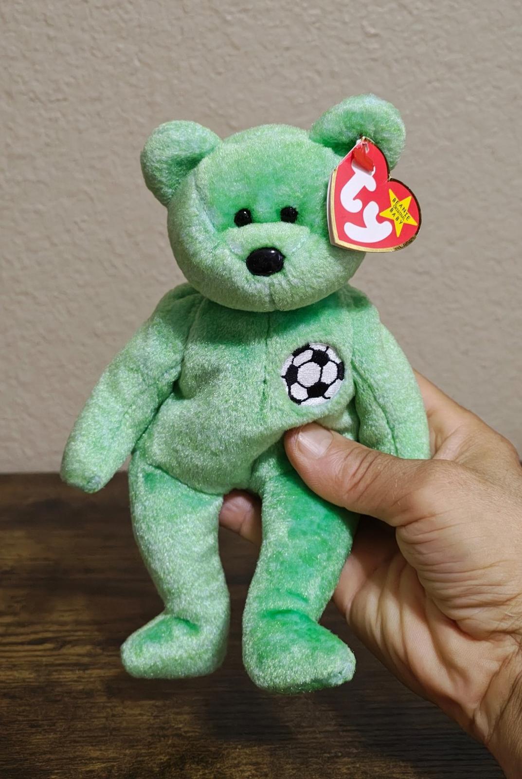 Green teddy bear plush with soccer ball patch and red TY heart tag held in hand.