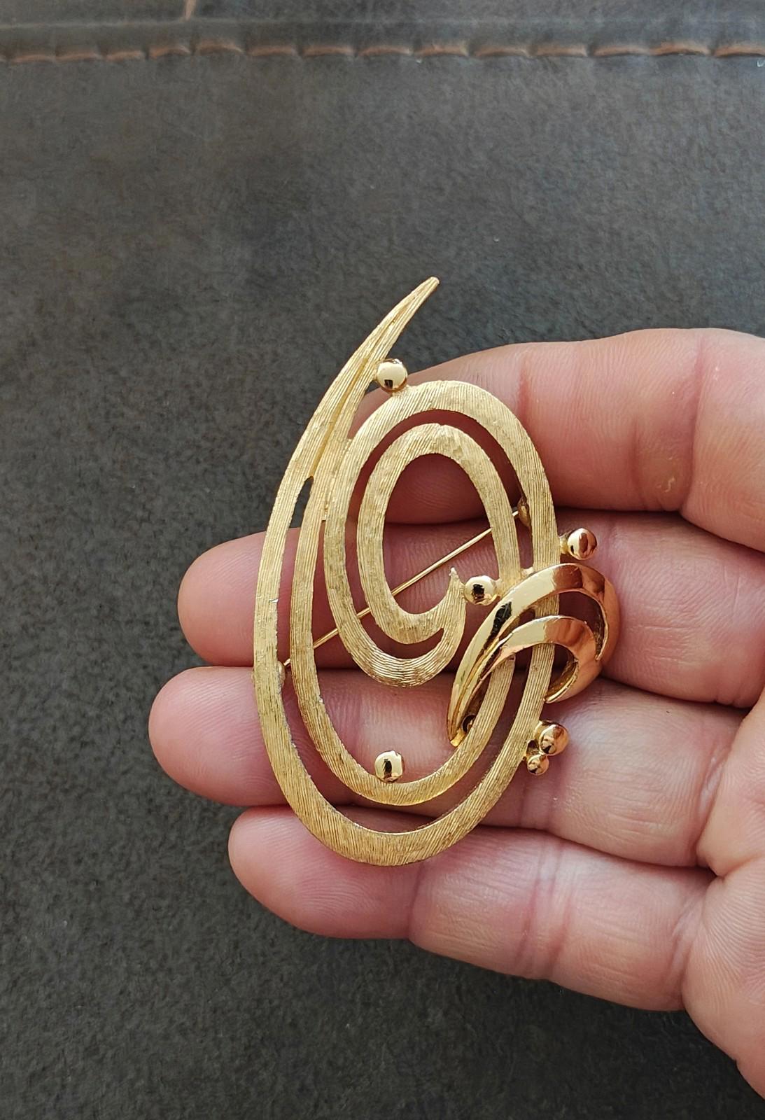 Gold tone oval brooch pin with double swirl detailing and pin clasp in view