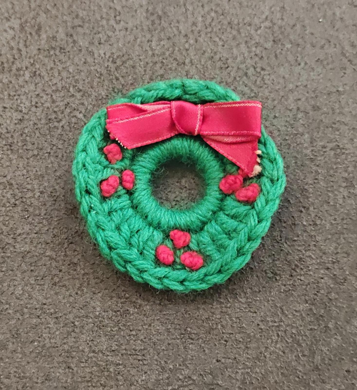 Green knitted wreath brooch with pink bow, red berry accents, round crocheted wreath