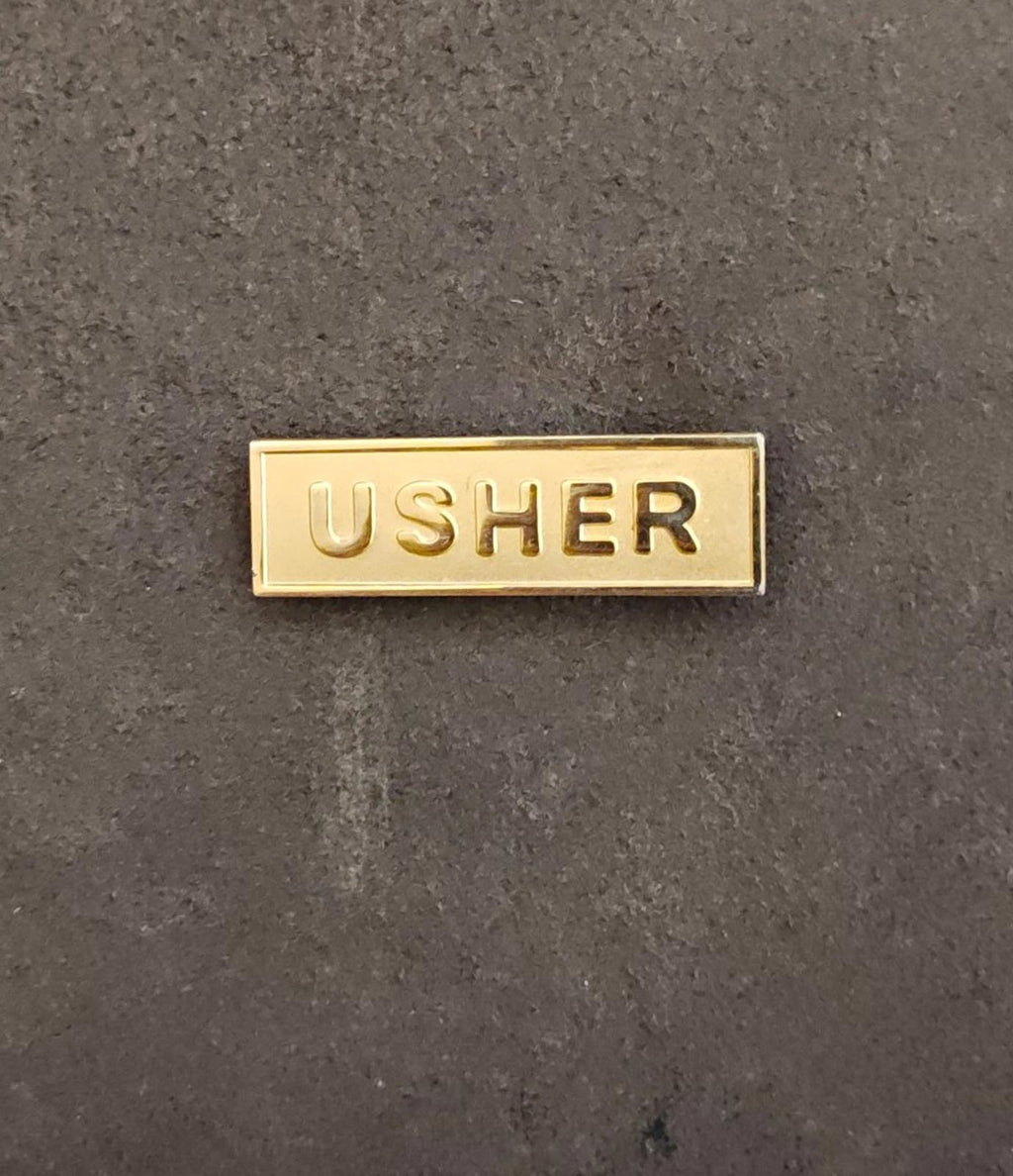 Gold tone USHER badge pin, centered rectangular design with embossed text