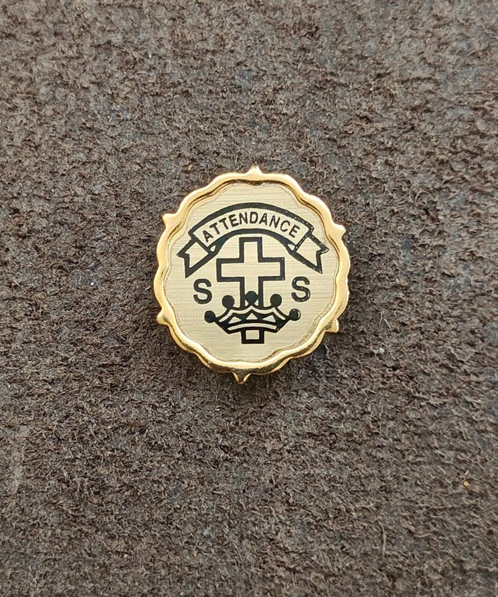 Gold-tone attendance pin with cross and crown emblem on a textured surface.