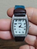 Ladies quartz wristwatch with rectangular white dial, crystal-accented bezel, DMQ logo