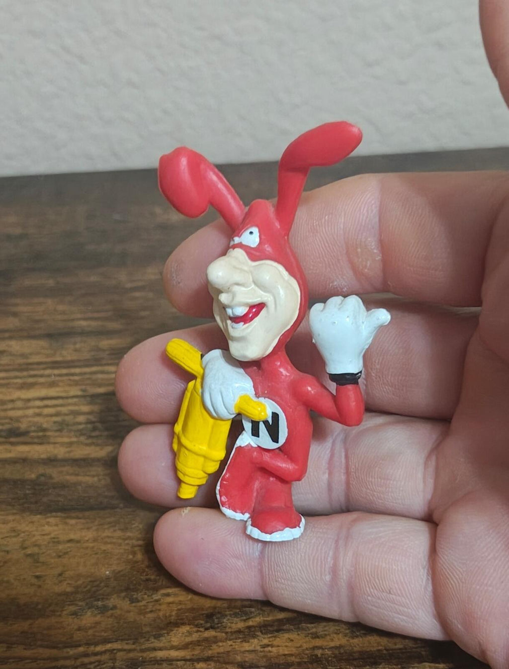 Red PVC cartoon Noid figure smiling in white shirt and red shoes, holding a white glove