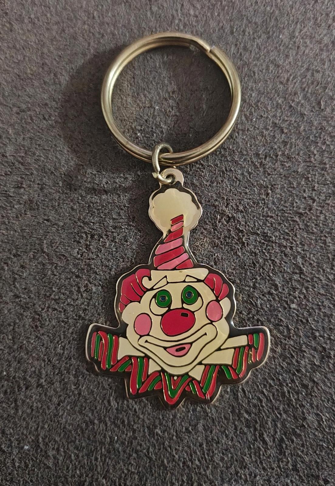 Gold-tone ring keychain with multicolor clown face charm on dark carpet