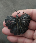 Silver-tone filigree butterfly brooch pin with raised wings and curved clasp prong