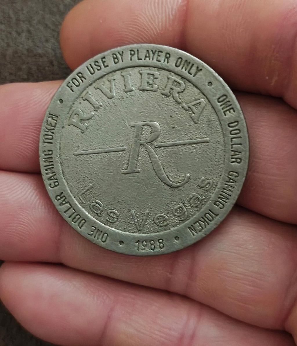 Silver one-dollar gaming token close-up held in hand, Riviera logo and one dollar text
