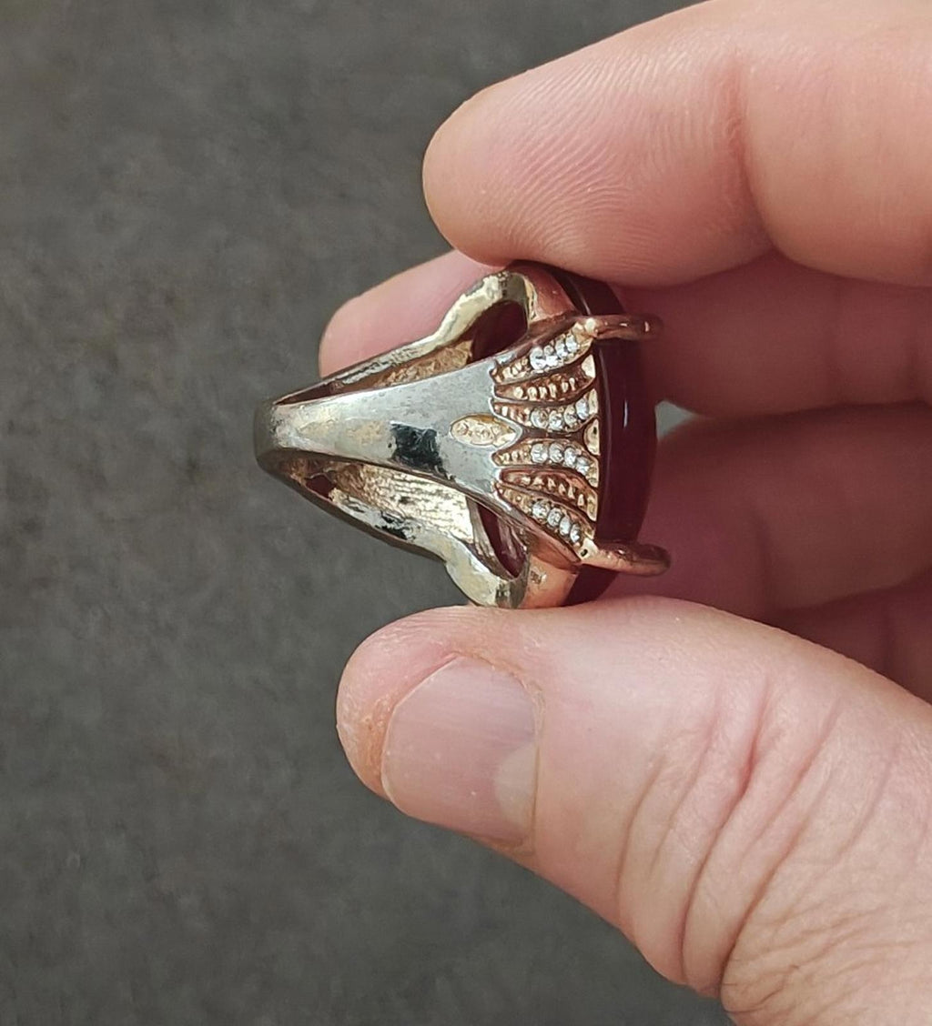 Gold-tone ring with red bezel and curved shoulders set with clear rhinestones