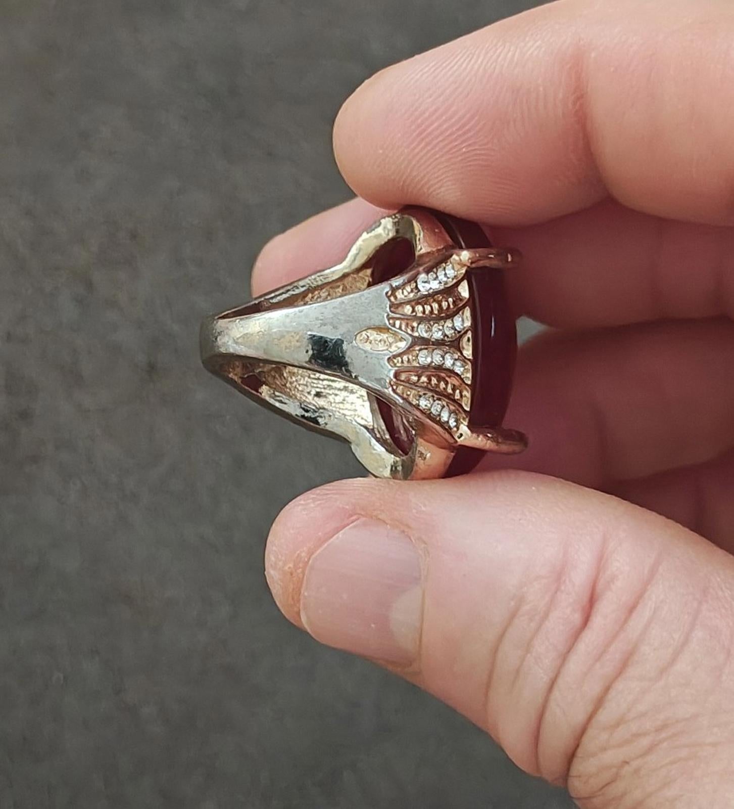 Gold-tone ring with red bezel and curved shoulders set with clear rhinestones