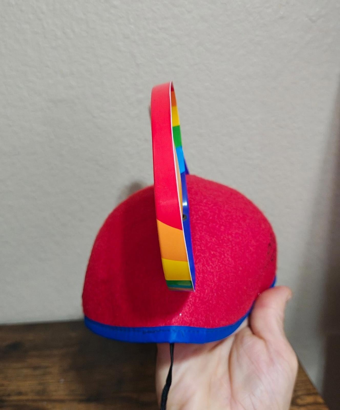 Side view of red felt Mickey Mouse ear hat with rainbow-striped ear and black cord